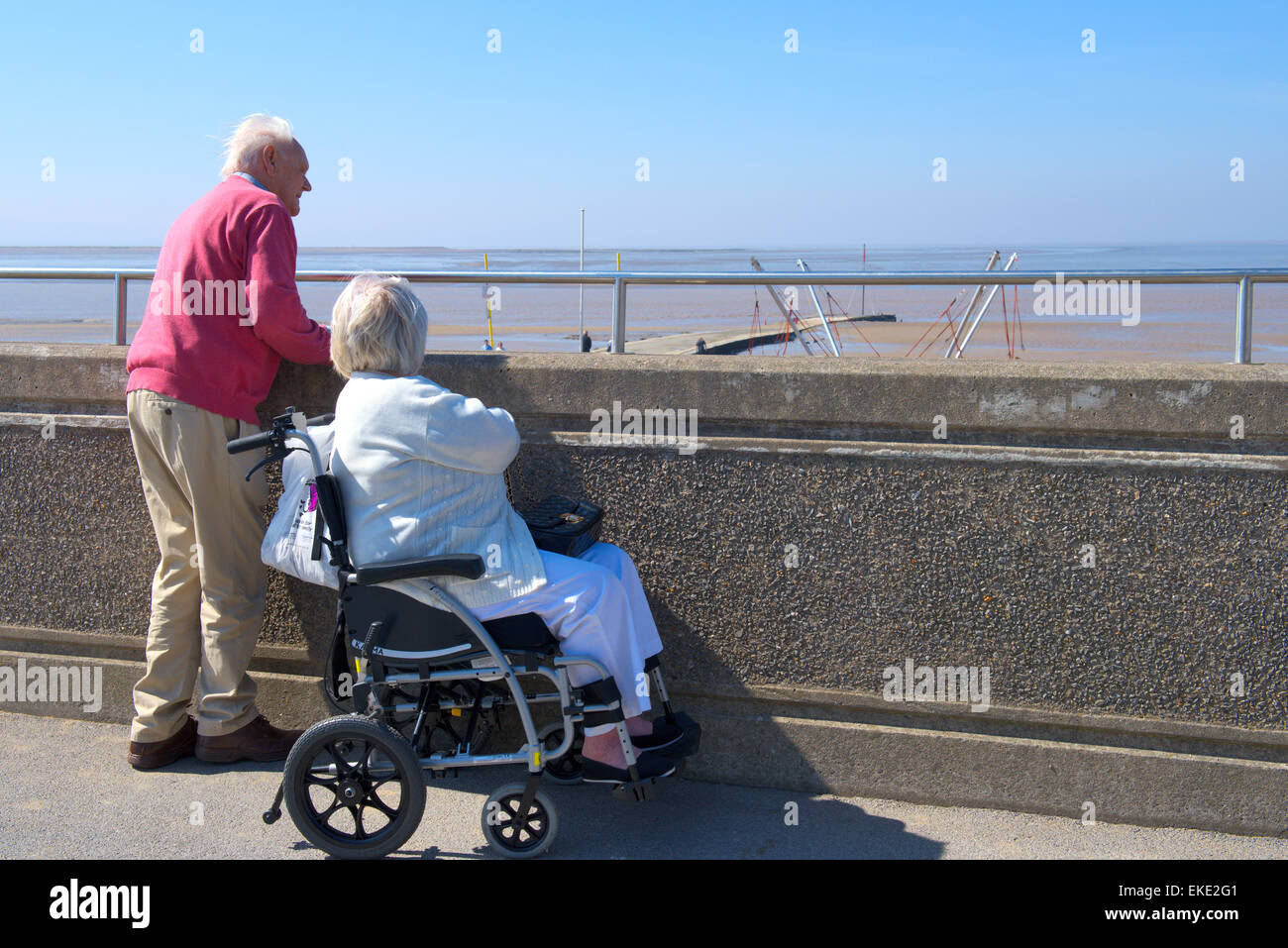 Pareja de ancianos mirando a lo largo de paseo a la playa de Muro Burnham-on-Sea, Somerset Foto de stock