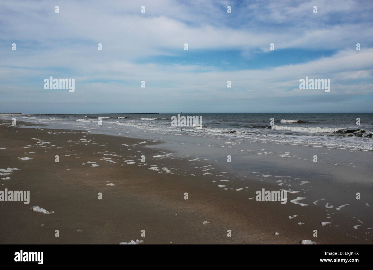 Una tranquila escena en la playa con un cielo azul y la espuma del mar Foto de stock