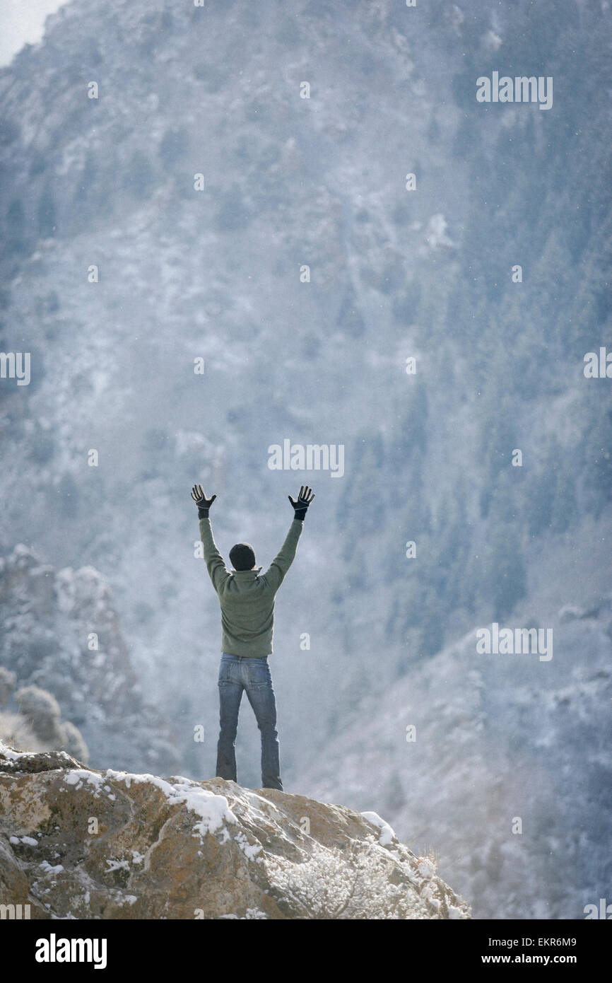 Un hombre saludo al sol, con los brazos levantados en un afloramiento rocoso en las montañas. Foto de stock