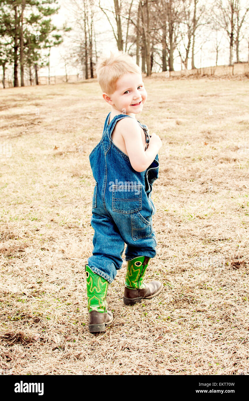 Boy en jeans overoles y botas, paseos en el país Foto de stock