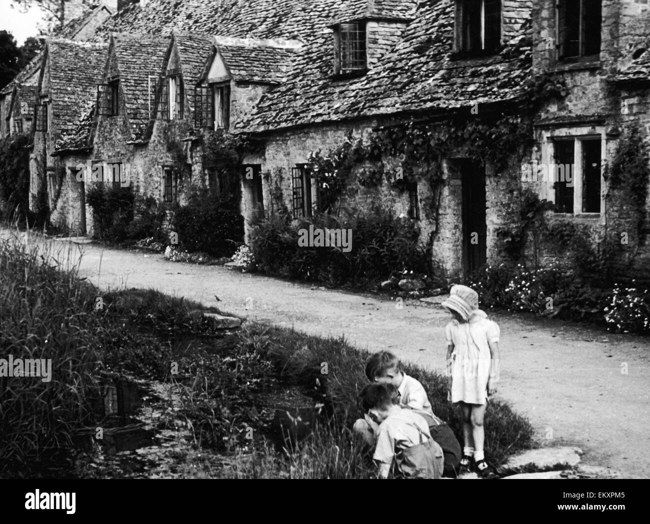 Niños jugando en la calle una fila de casitas pintorescas en Arlington fila en la aldea de Cotswold Bibury, Gloucestershire. Circa 1935. Foto de stock