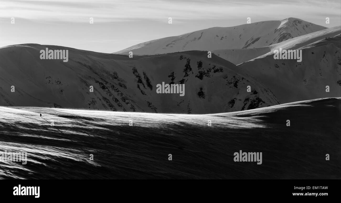 La fotografía en blanco y negro y fuerte tormenta, una persona va en altas cadenas montañosas cubiertas de nieve, desde el hombre cae una larga sombra Foto de stock
