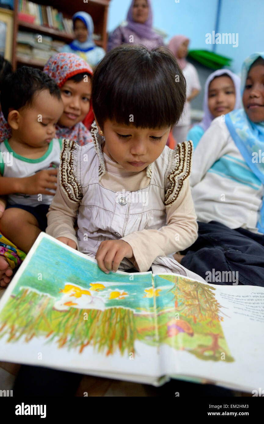 Chica mirar un libro de imágenes, Gampong Nusa village, Aceh, Indonesia Foto de stock