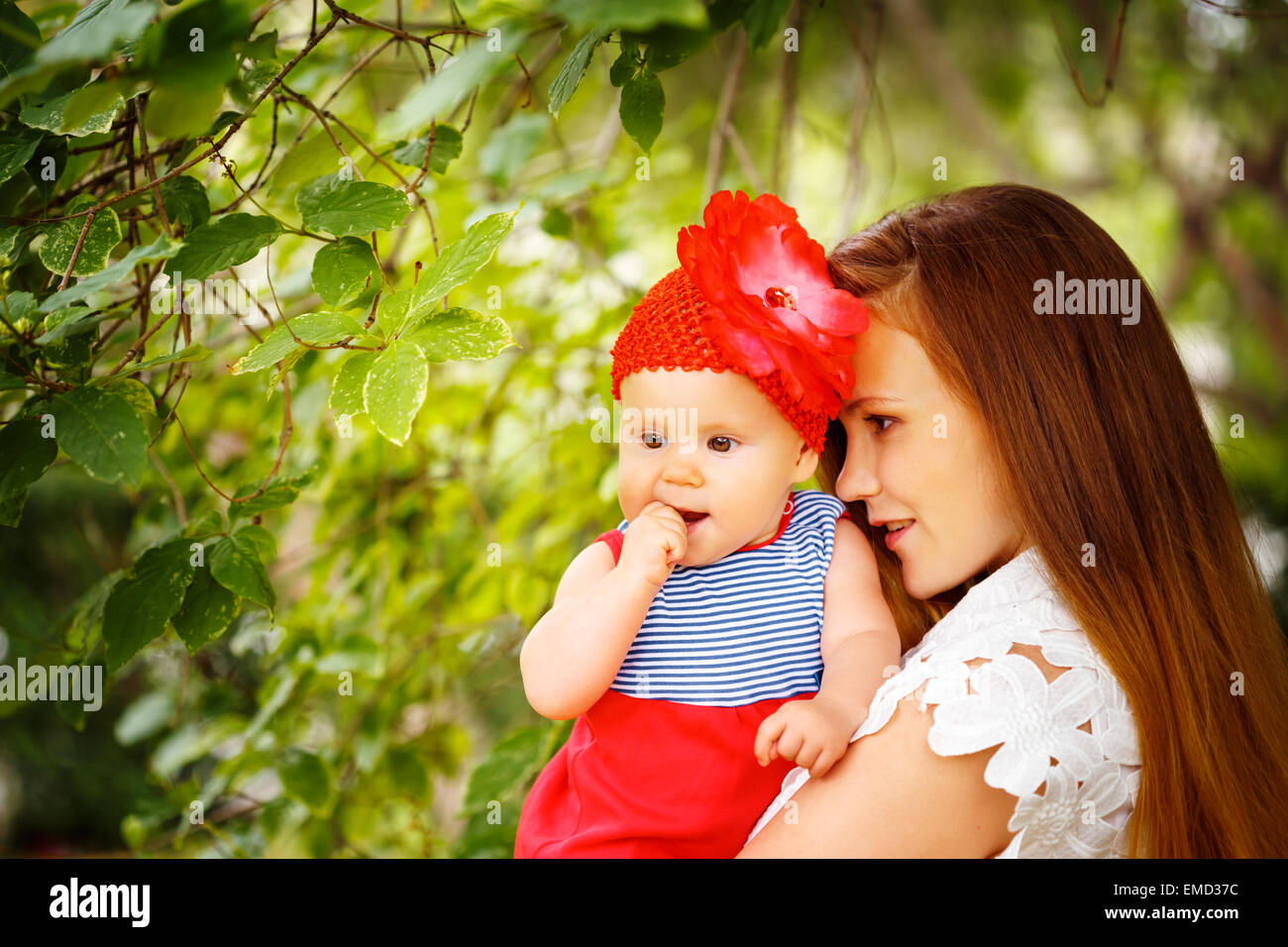 Ligero Th Reverberación Hermosa mujer sosteniendo lindo bebé niño curioso en ropa de color rojo.  Relajarse en el verde parque de verano Fotografía de stock - Alamy