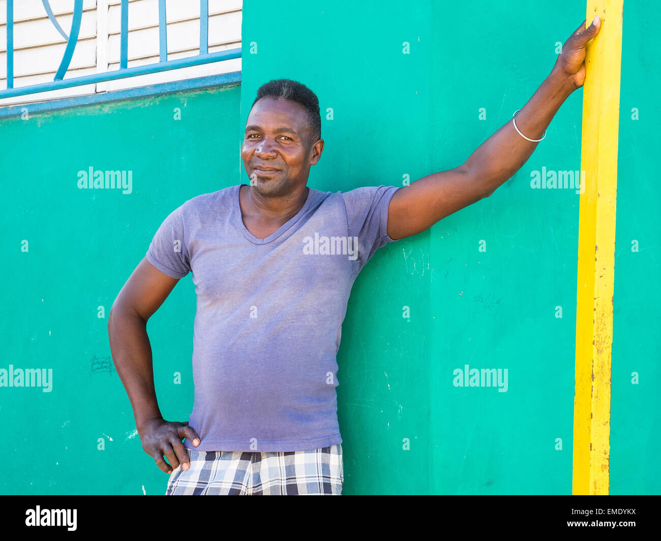 Un hombre afrocubano se inclina con su brazo contra paredes de colores brillantes de la parte exterior de las casas vecinas. Foto de stock