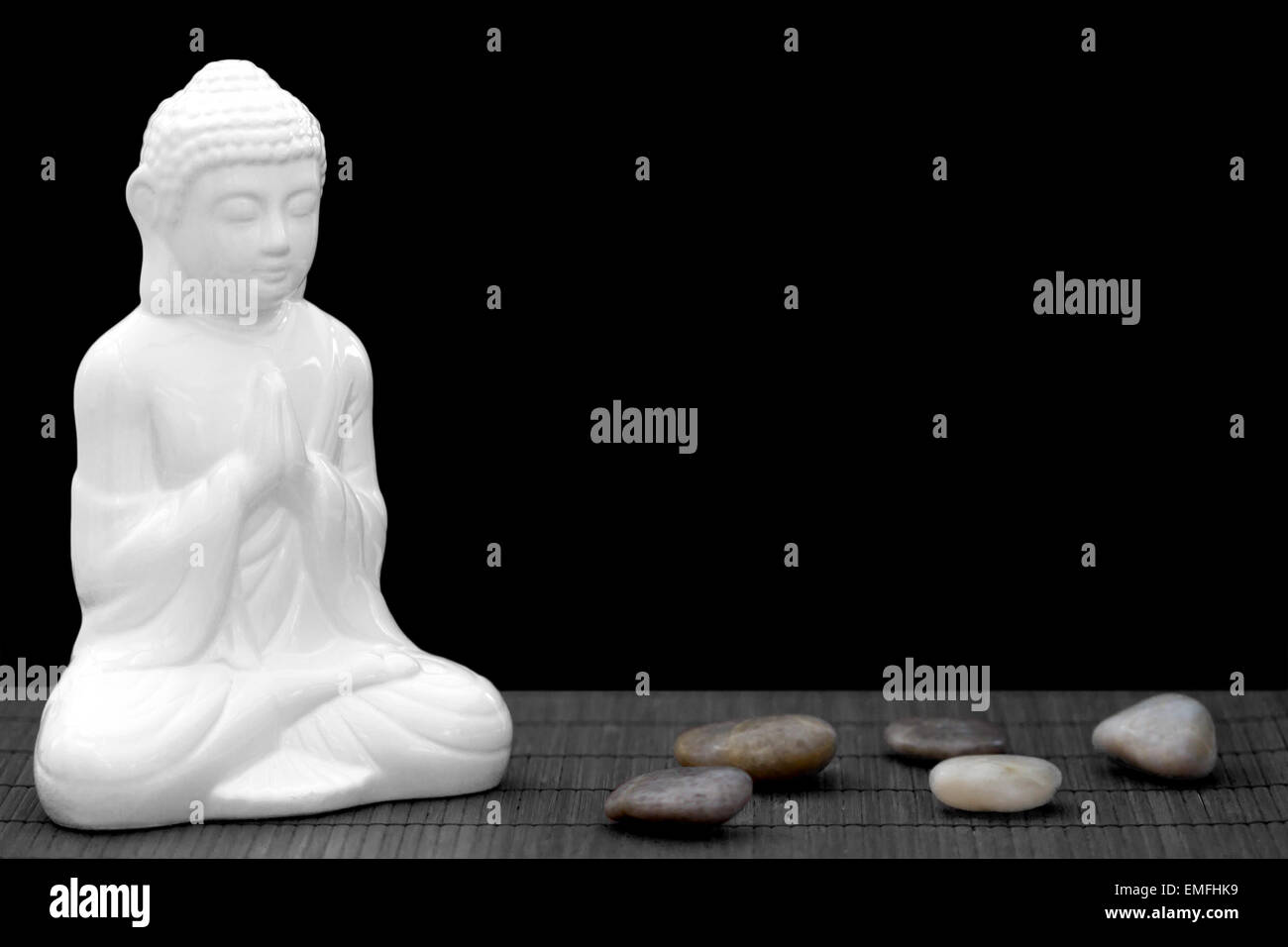 Figura blanca en pose de meditación con cantos rodados Foto de stock