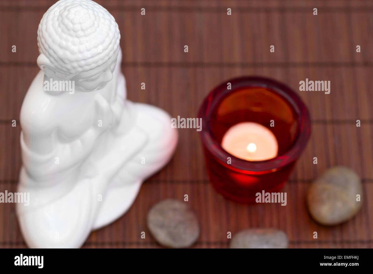 Figura blanca en pose de meditación con cantos rodados y vela en vidrio rojo desde arriba Foto de stock