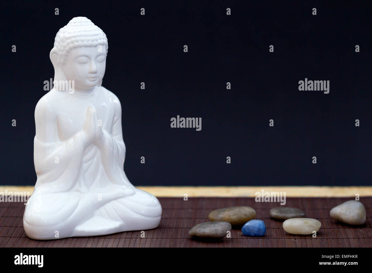 Figura blanca en pose de meditación con cantos rodados y una piedra azul Foto de stock