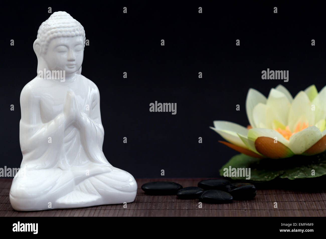 Figura blanca en pose de meditación con guijarros y agua lilly en fondo borroso Foto de stock