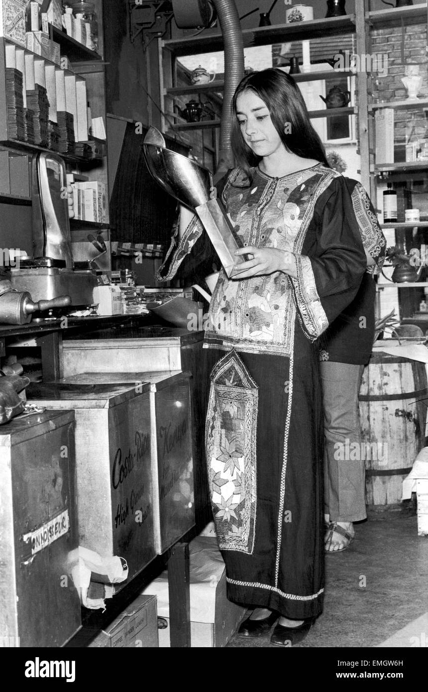 Minnie King, directora de una tienda de comida de salud en Hampstead, sirve a un cliente algunos granos de café fresco vestidos de traje tradicional indio. El 4 de octubre de 1970. Foto de stock