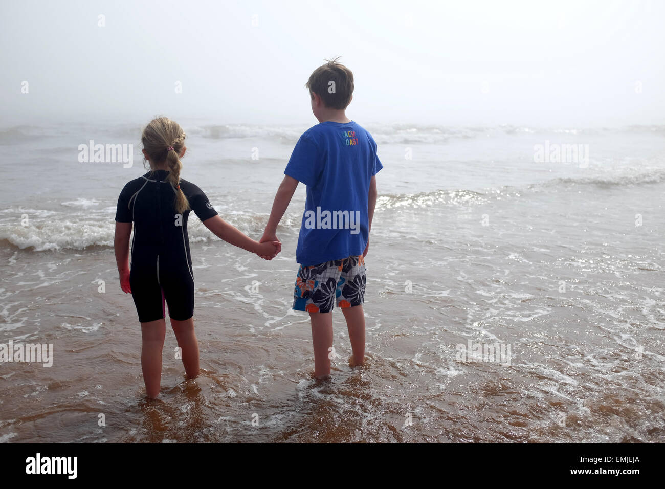 Un chico y una chica cogidos de la mano mire hacia el mar en un día brumoso Foto de stock