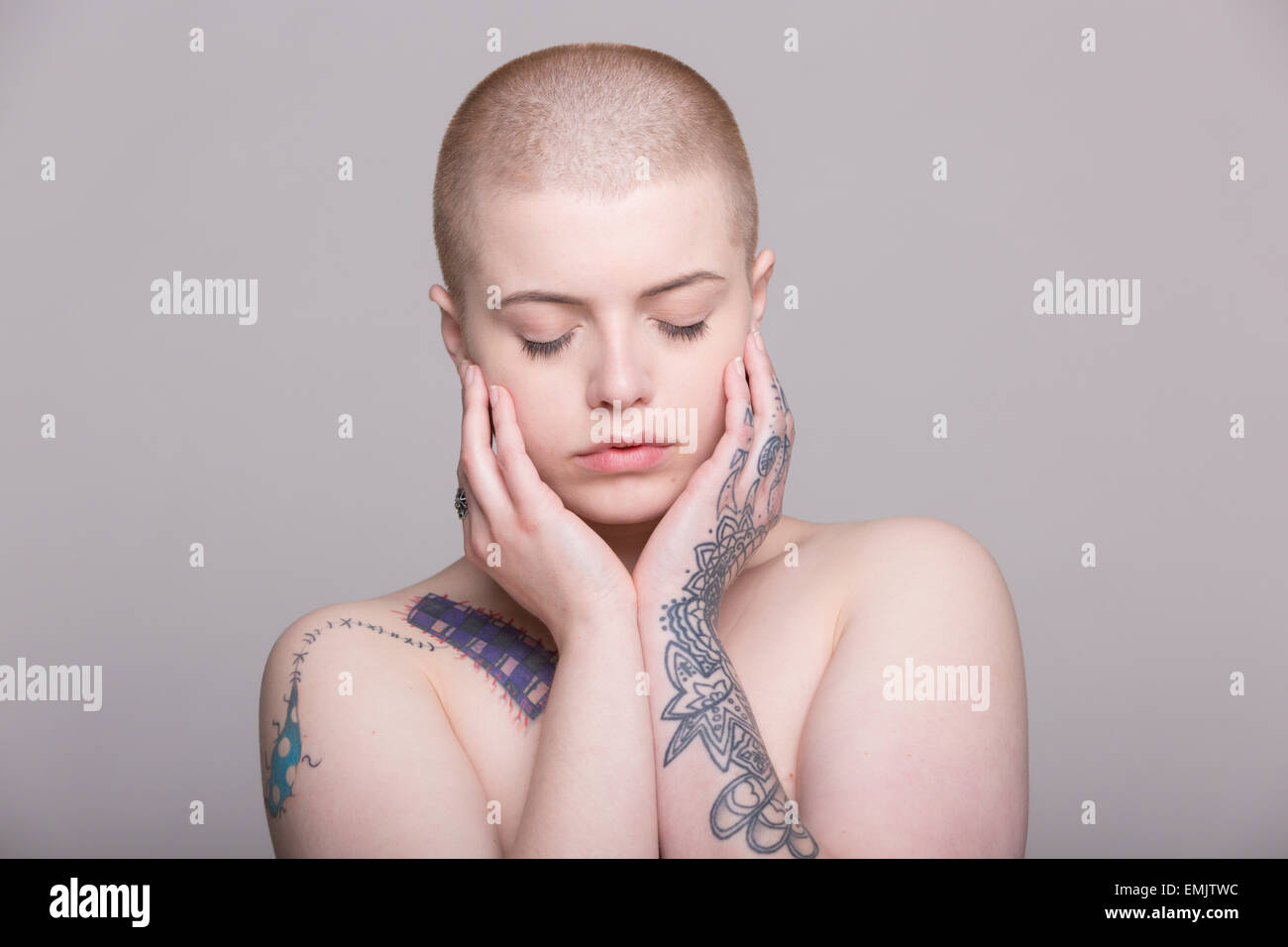 Una mujer joven con la cabeza rapada y tatuajes sobre su hombro, brazos y manos Foto de stock
