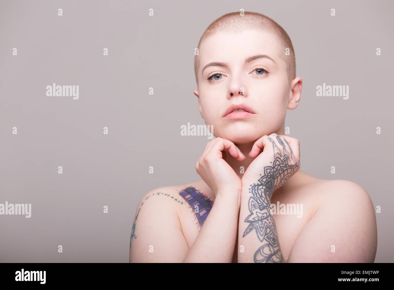 Una mujer joven con la cabeza rapada y tatuajes sobre su hombro, brazos y manos Foto de stock
