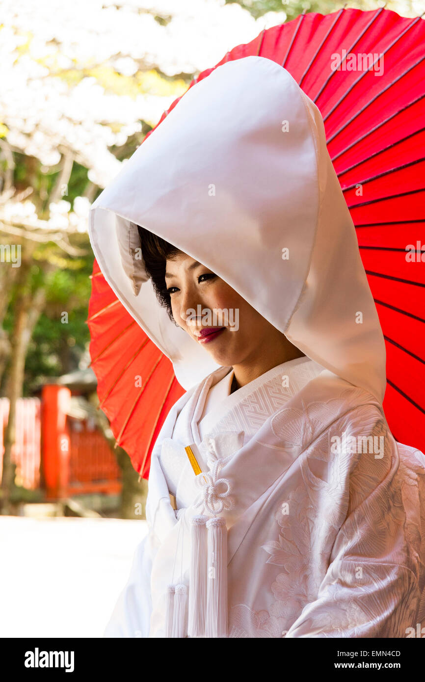 Japón, Nara, Tamukeyama santuario. Novia sentada en el tradicional japonés shiromuku kimono blanco, sonriendo con sombrilla roja, paraguas de papel detrás de ella. Foto de stock