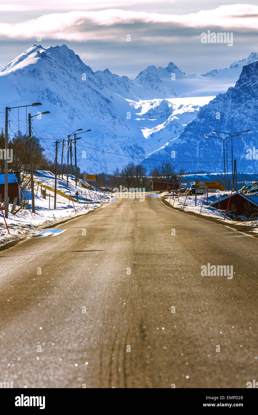 Un soleado paisaje noruego con un camino abierto en primer plano y con nieve y montañas azules en el fondo. Foto de stock