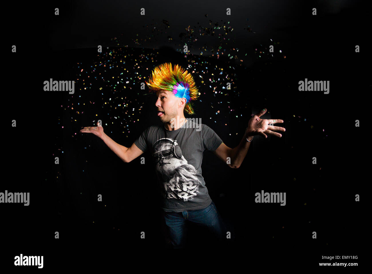 Retrato de un hombre con cabello colorido lanzando confeti en el aire. Foto de stock