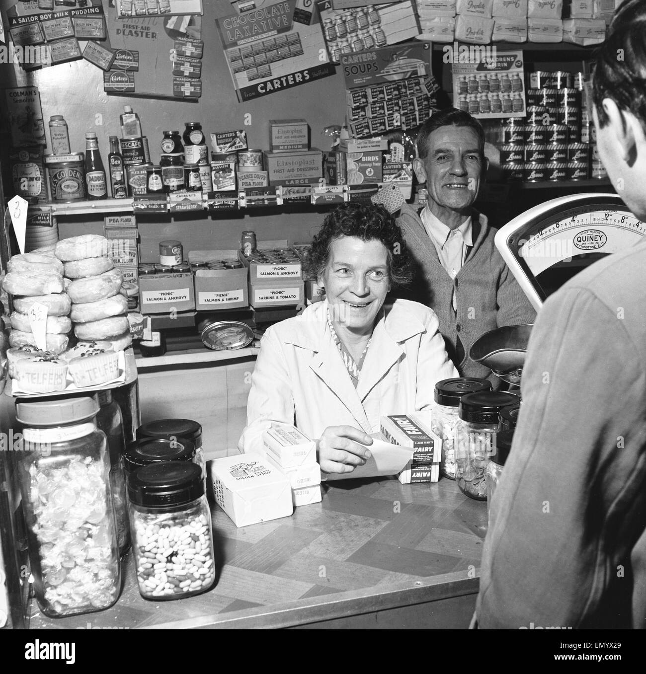 Almacenero local y su esposa visto aquí sirve a un cliente. El 14 de noviembre de 1955 Foto de stock