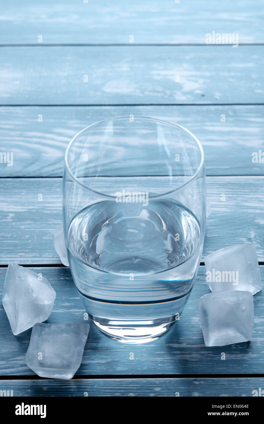 Vaso de agua y cubitos de hielo derritiéndose sobre una tabla de madera Foto de stock