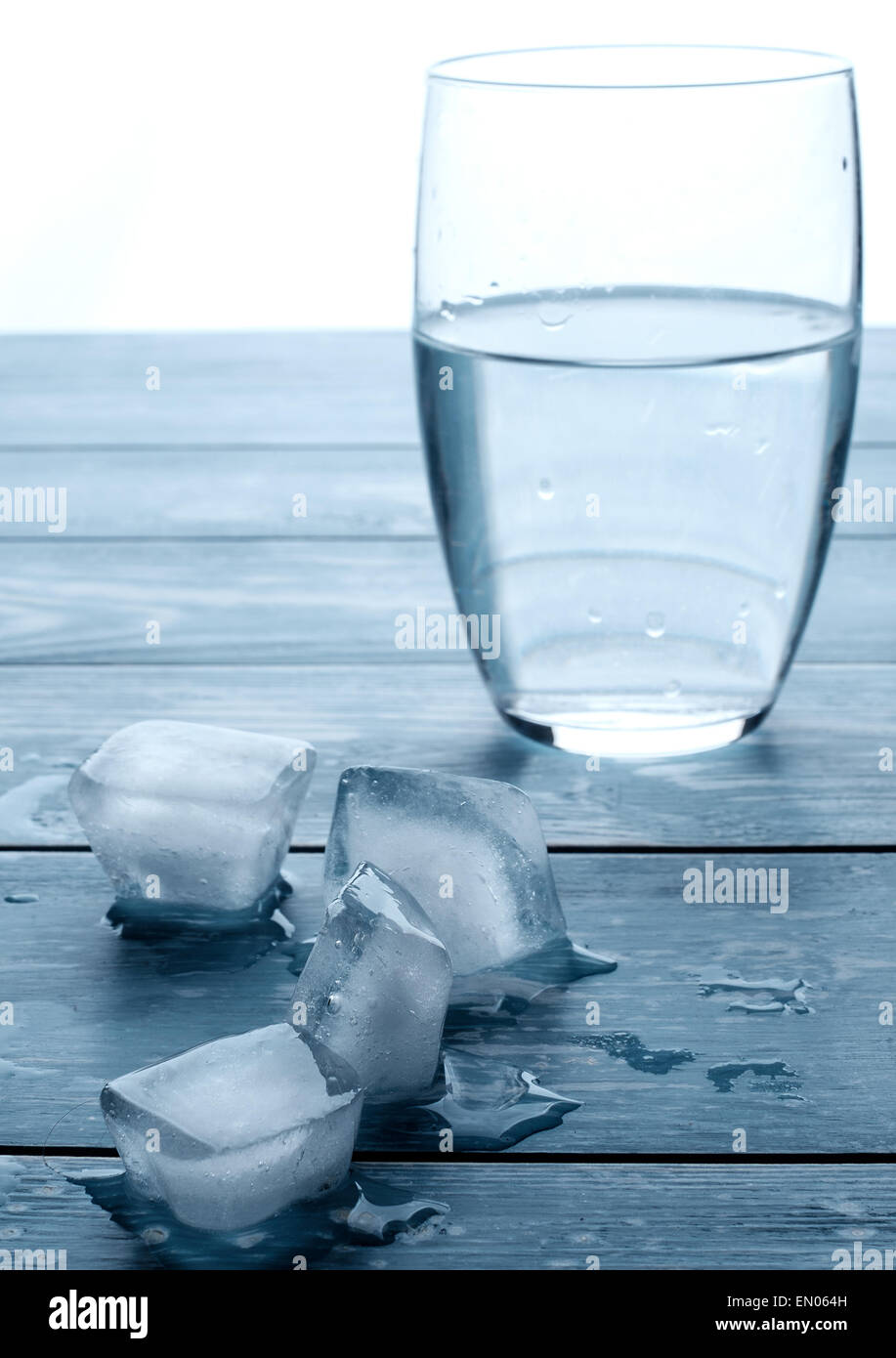 Vaso de agua y cubitos de hielo derritiéndose sobre una tabla de madera Foto de stock