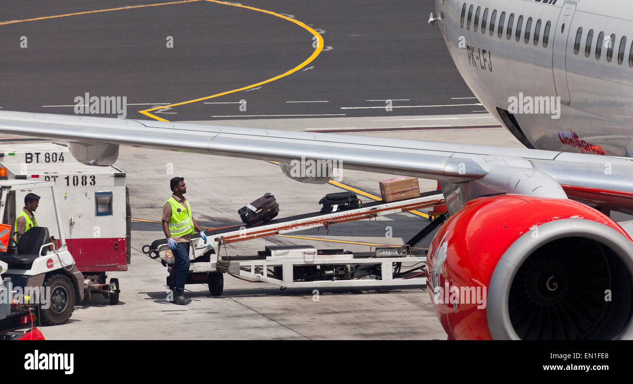 Del lado aire del aeropuerto, personal de mantenimiento, carga de equipaje de los pasajeros en un avión espera utilizando un sistema de cinta transportadora Foto de stock