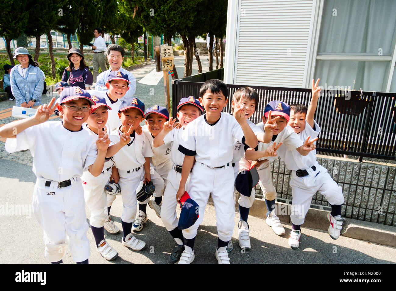 Grupo de niños pequeños, chicos, de 7-10 años, un equipo de béisbol que se posan para el espectador, sonriendo y dando dos gestos de paz con los dedos. Foto de stock