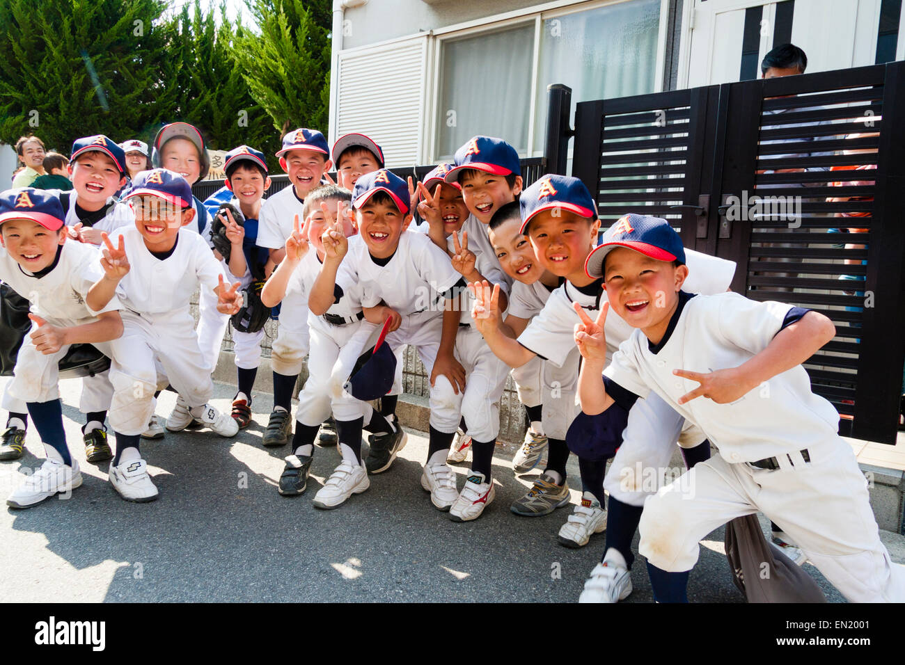 Grupo de niños pequeños, chicos, de 7-10 años, un equipo de béisbol que se posan para el espectador, sonriendo y dando dos gestos de paz con los dedos. Foto de stock