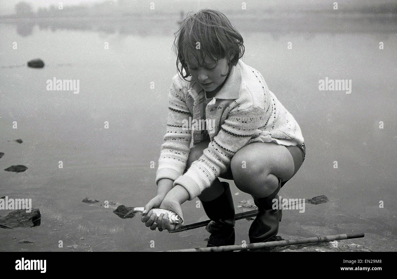 1960 histórico, joven al borde del agua tiene en sus manos un pequeño pez que acaba atrapada. Foto de stock