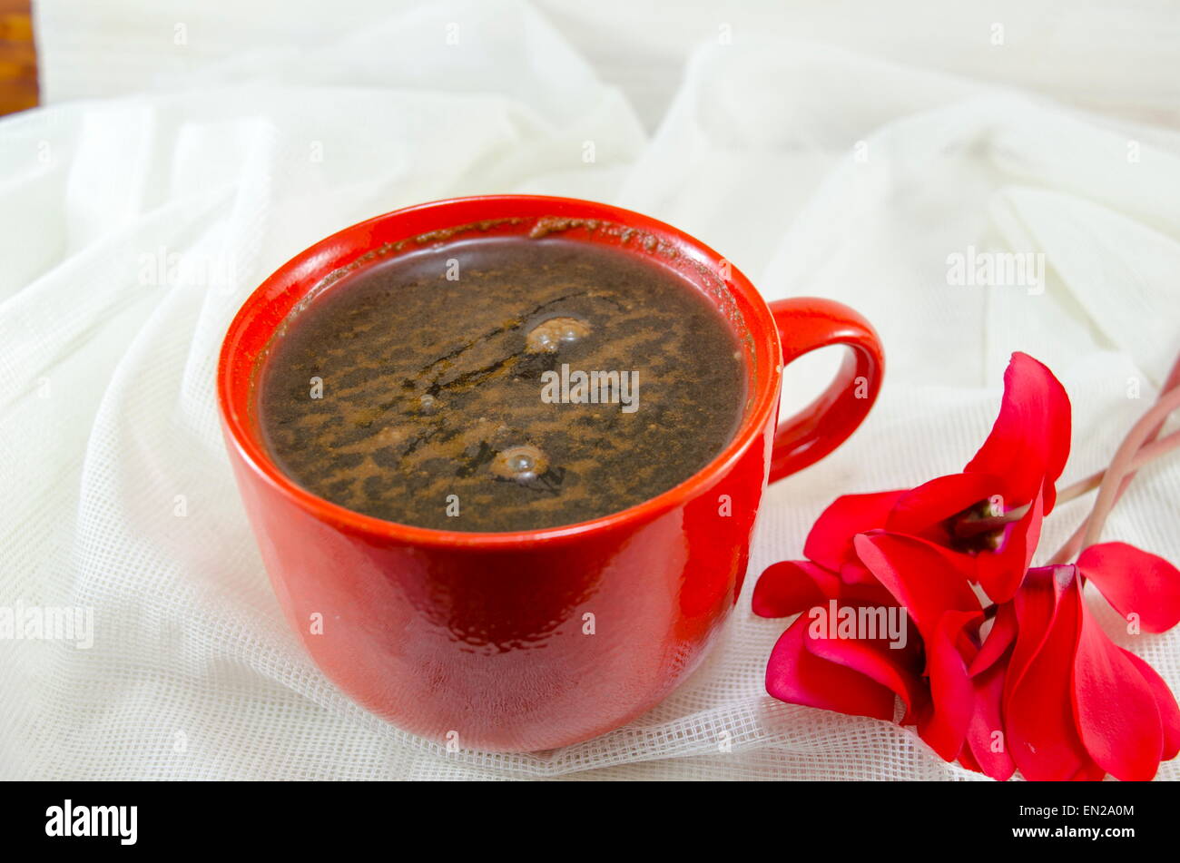 Taza de café rojo decorado con espuma y una flor en un romántico vintage un mantel. Foto de stock