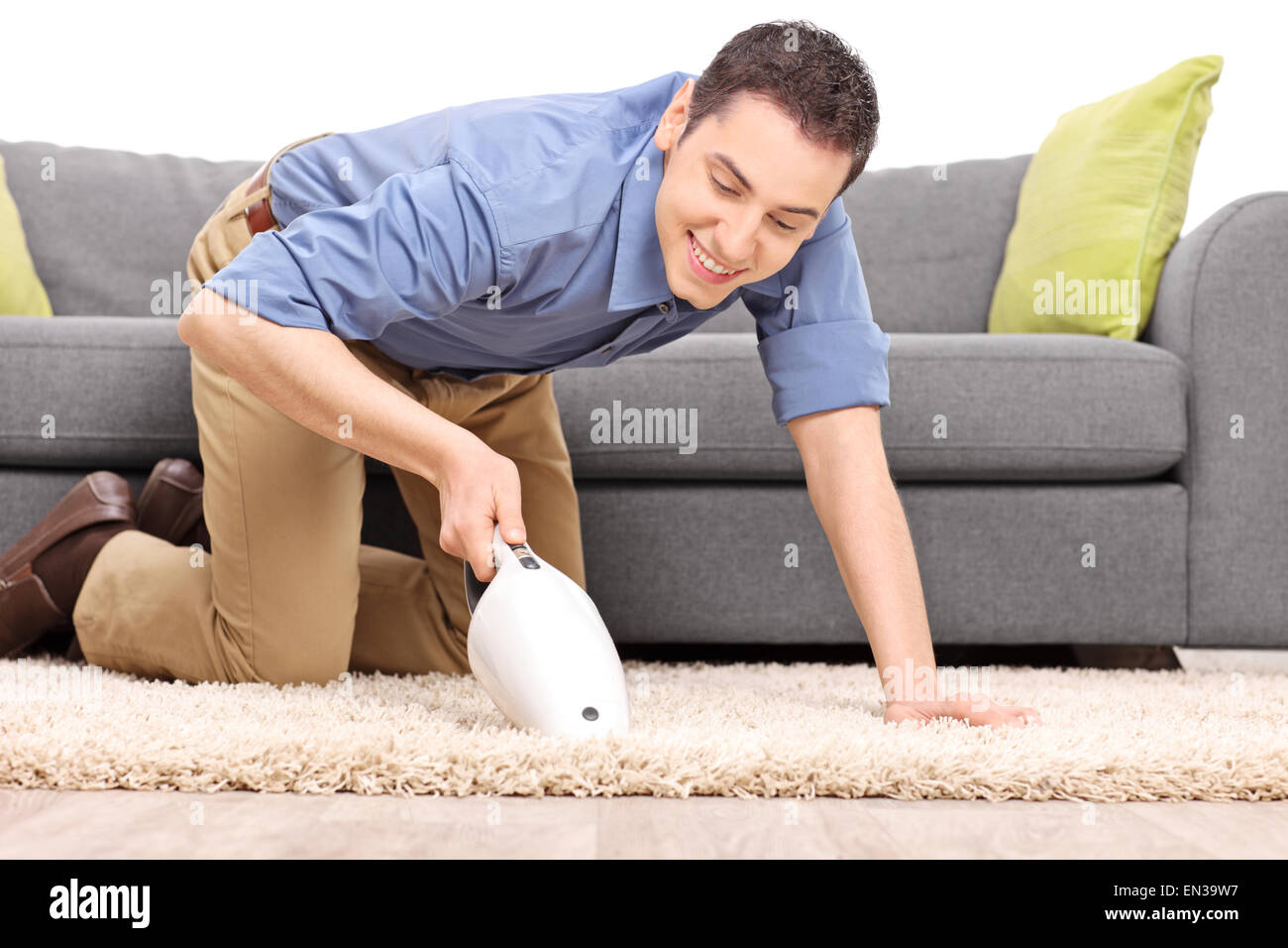 Joven Hombre alegre aspirar una alfombra con un aspirador de mano aislado sobre fondo blanco. Foto de stock