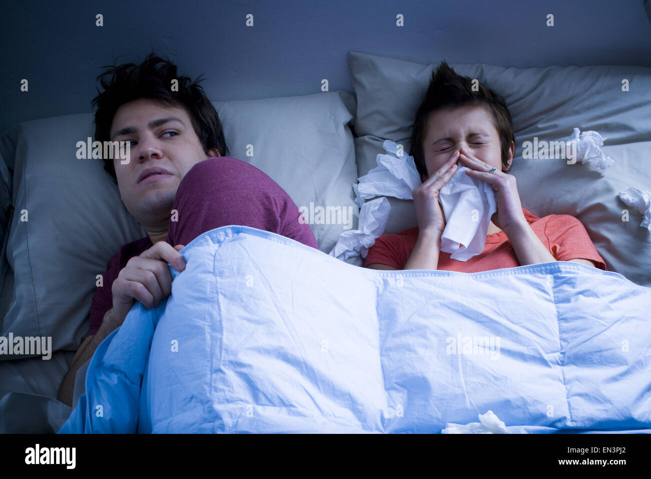El hombre tendido en la cama con una mujer sonarse la nariz con un pañuelo Foto de stock