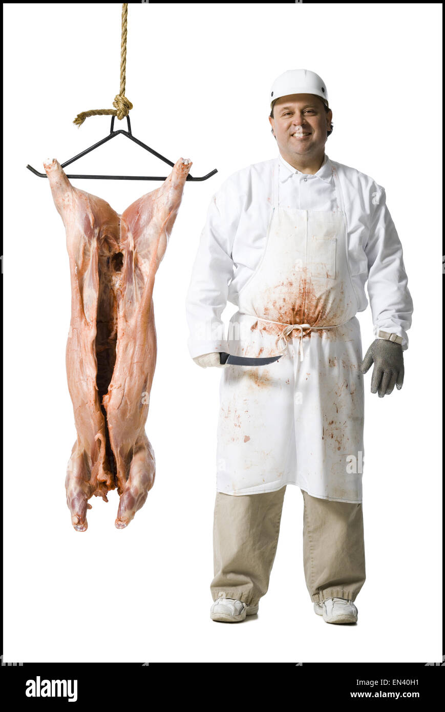 El carnicero de pie con la cuchilla y carcasa colgante Foto de stock