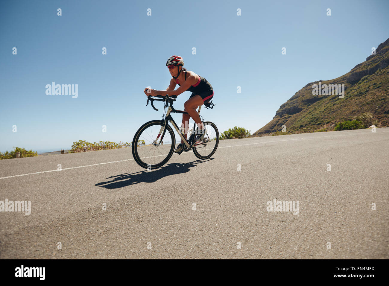 Imagen de la mujer joven en bicicleta por las carreteras del país. Colocar atleta femenina montando en bicicleta cuesta abajo. Mujer realizando entrenamiento ciclismo. Foto de stock
