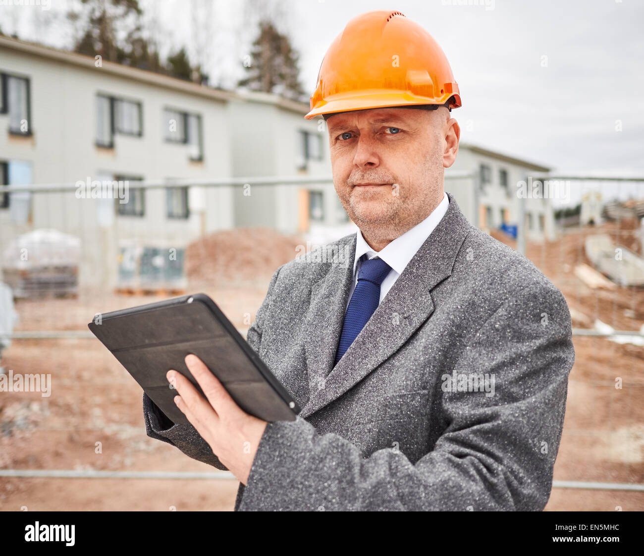 Ingeniero macho utiliza tablet pc, vistiendo el traje y el sombrero duro, construcción de casas en segundo plano del sitio Foto de stock