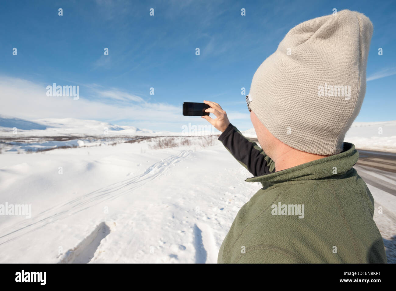 El hombre toma una foto con el iPhone de montañas y desierto por carretera, Kilpisjärvi, Laponia, Finlandia Foto de stock