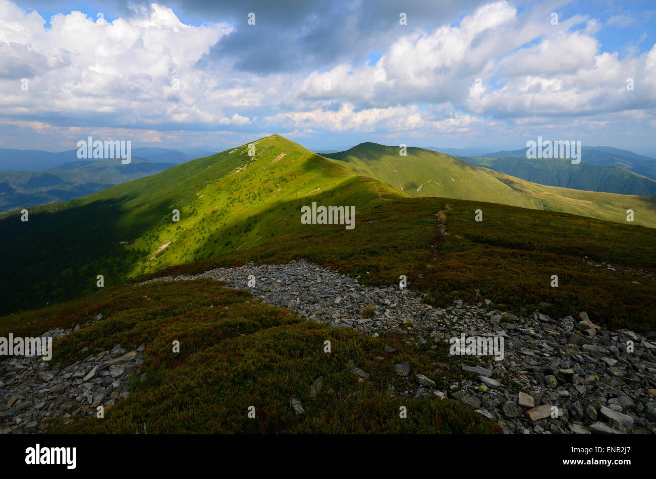 Cordillera con verdes colinas cubiertas de hierba y manchas luminosas y rocas en primer plano Foto de stock