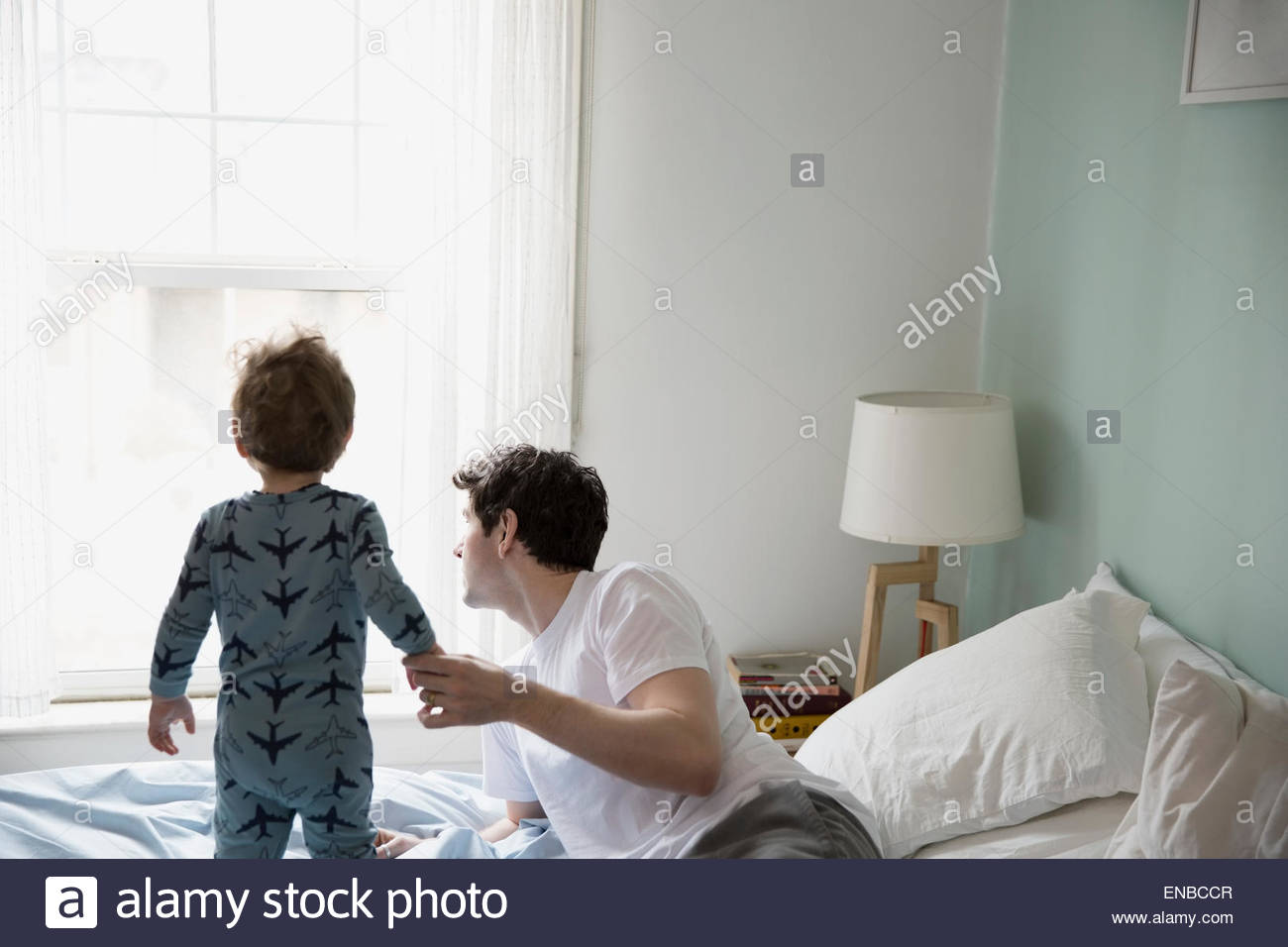 Padre e hijo en pijama mirando por la ventana Foto de stock