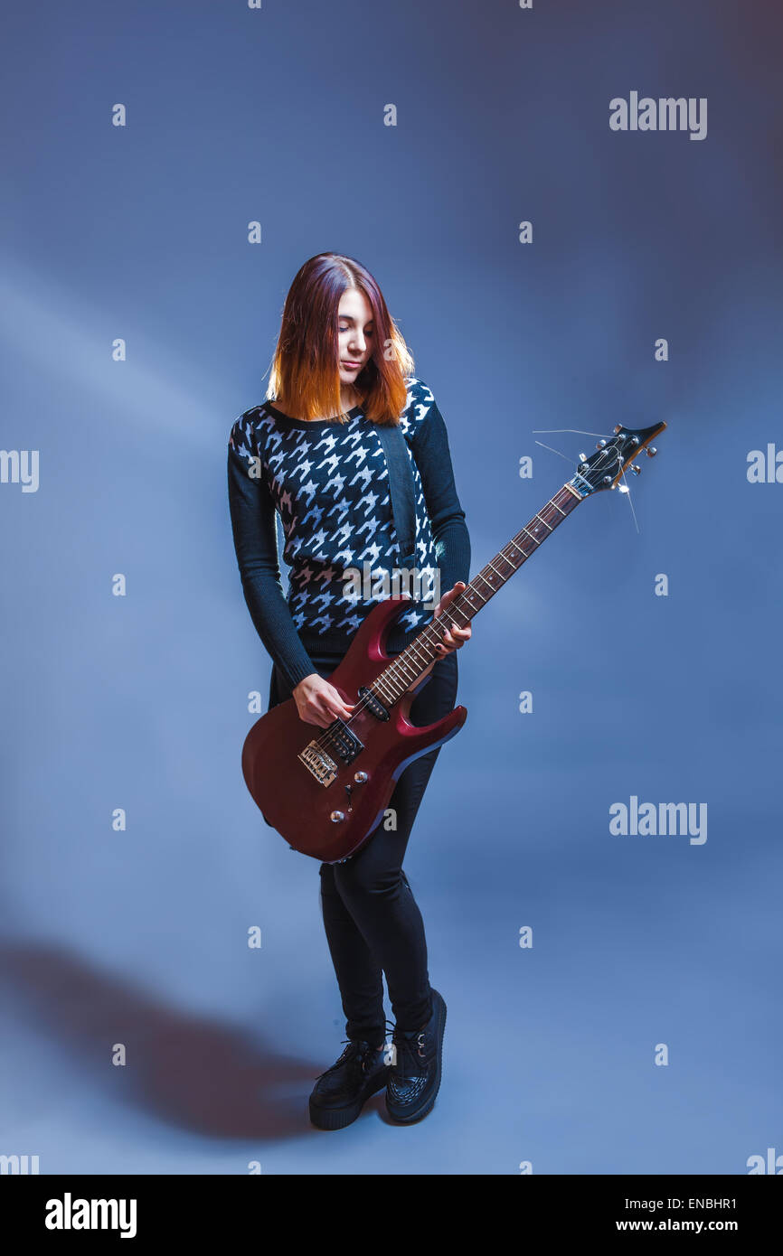Chica rubia de aspecto europeo en jersey azul la guitarra sobre un fondo gris, la nostalgia, la tristeza Fotografía de stock -