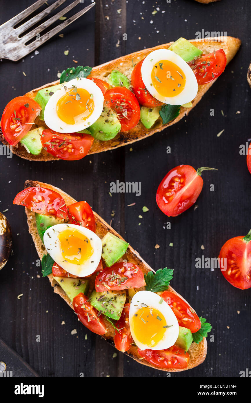 Bruschetta con tomate, aguacate y huevo de codorniz sobre una tabla de madera Foto de stock