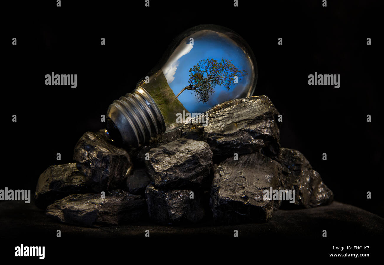 Una imagen creativa de la energía de la tierra representada por el cielo azul y un árbol dentro de una lámpara colocada sobre un montón de carbón Foto de stock