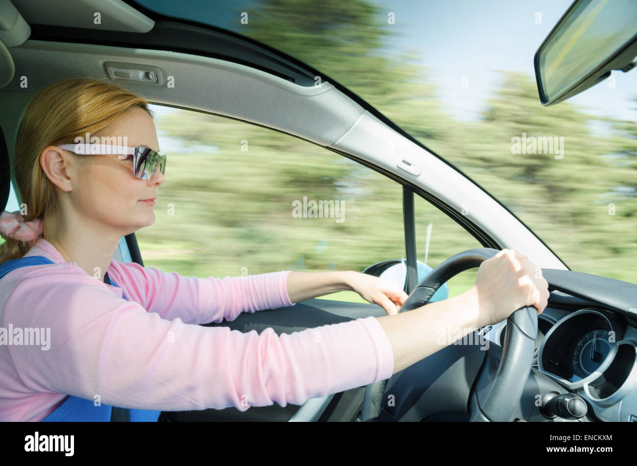 Pretty Woman en gafas de sol de conducción rápida de coches con parabrisas panorámico. En Alta velocidad de obturador lento movimiento borrosa en el fondo. Foto de stock