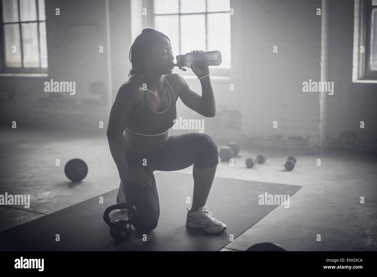 Botella de agua potable de la mujer negra en la oscuridad gimnasio Foto de stock