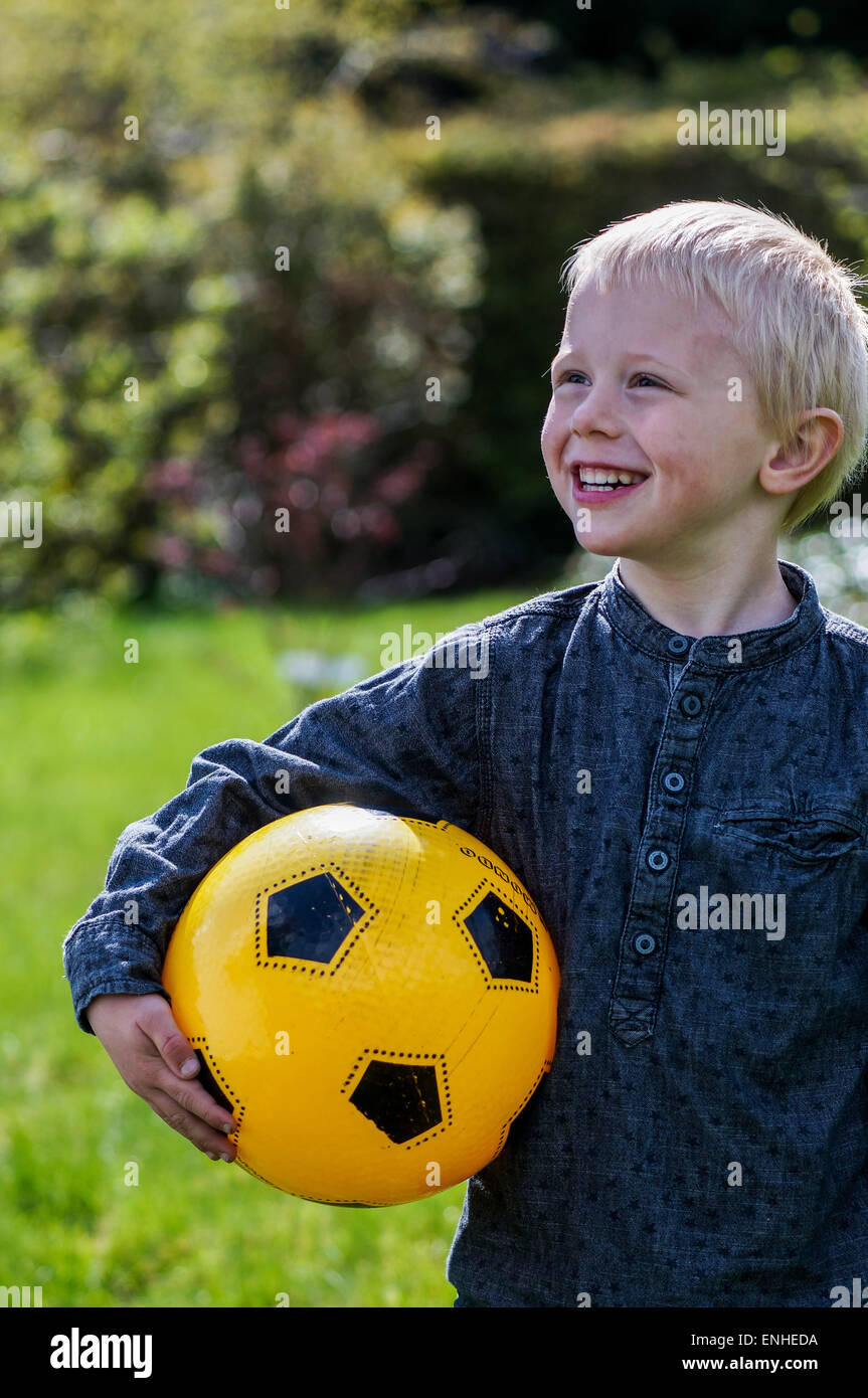 Niños preescolares con el fútbol, balón de fútbol. Muchacho que está en el jardín con su pelota de fútbol . Su fútbol es amarillo. Viste Foto de stock