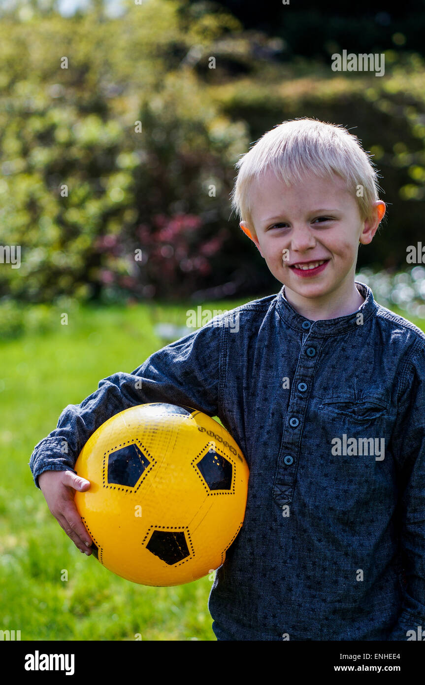 Niños preescolares con el fútbol, balón de fútbol. Muchacho que está en el jardín con su pelota de fútbol . Su fútbol es amarillo. Viste Foto de stock