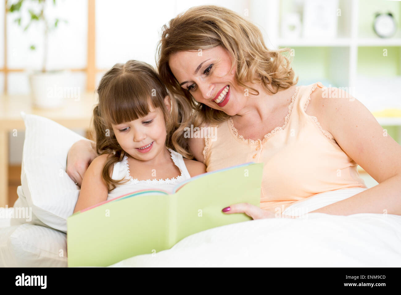 Madre e hija feliz leer juntos un libro en la cama Foto de stock