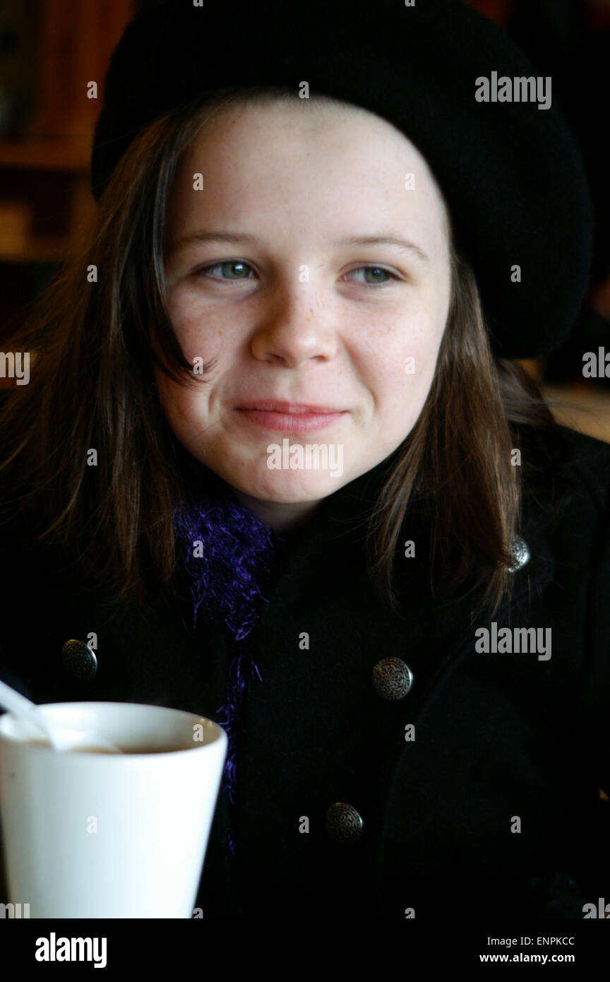 Adolescente disfrutando de una bebida caliente de té o café caliente vestida con ropa de invierno con un abrigo, sombrero y bufanda. Foto de stock