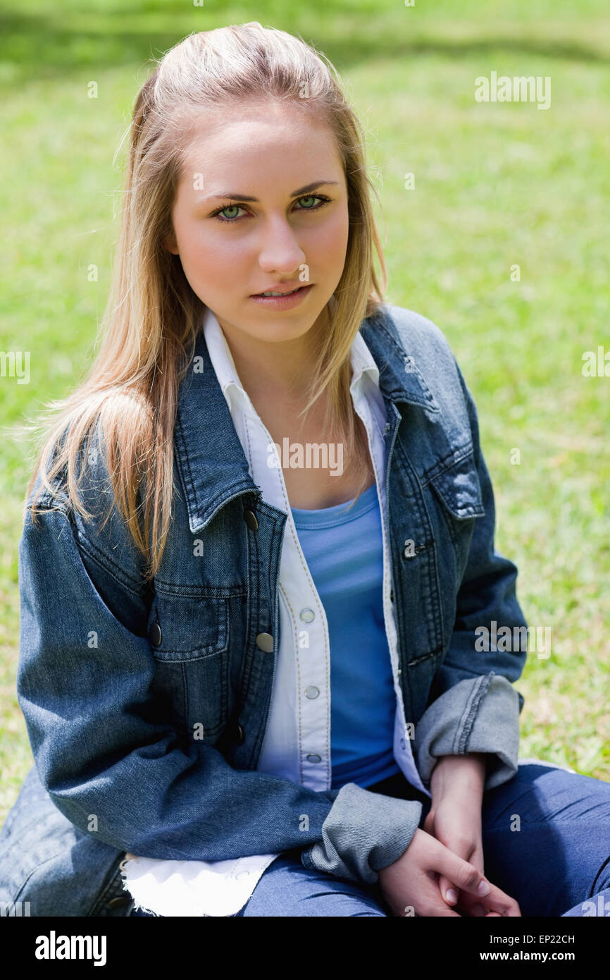 Grave joven muchacha sentada sobre la hierba mirando a la cámara Foto de stock