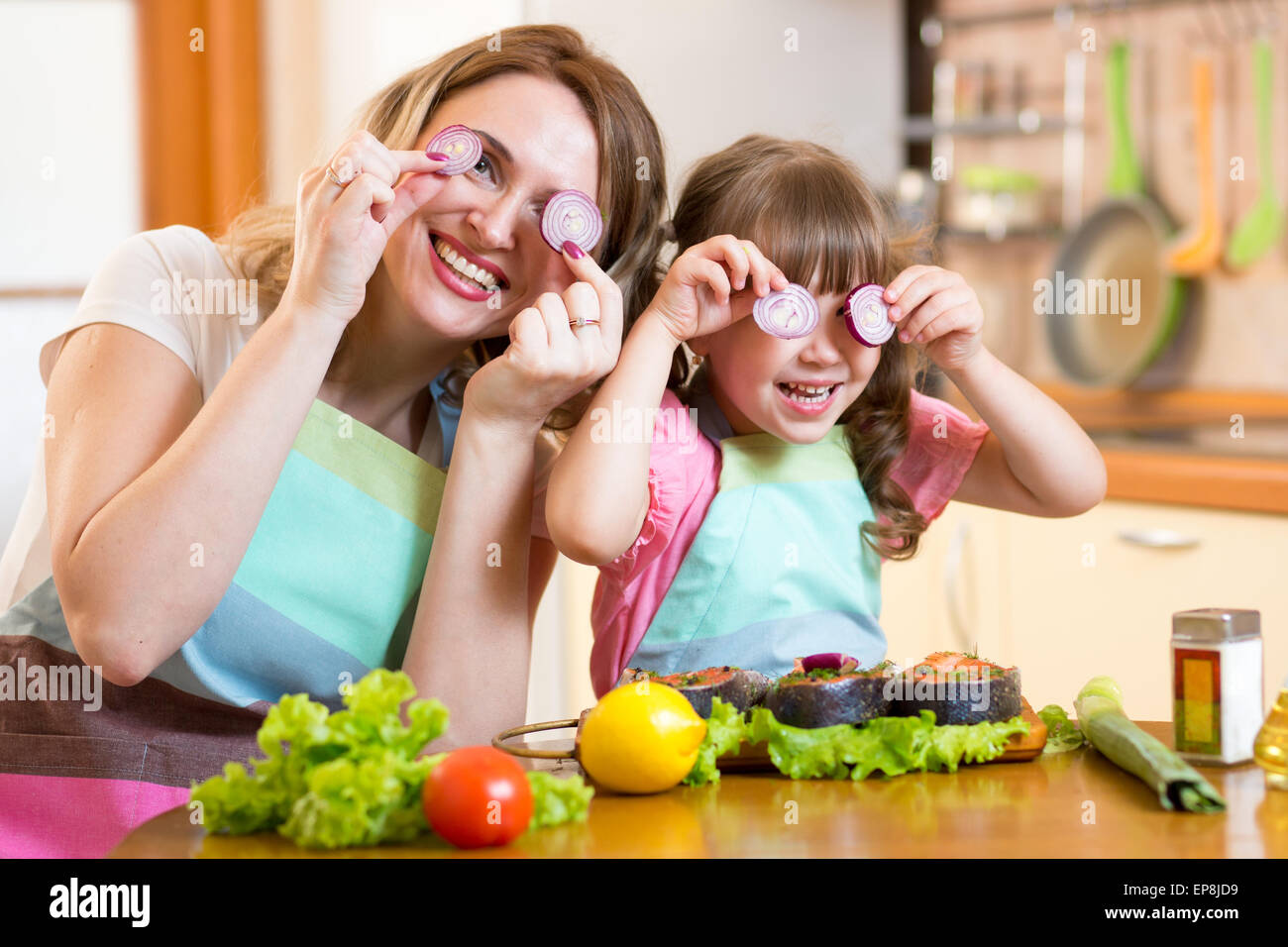 Madre e hija jugando con las verduras en la cocina, la comida sana Foto de stock