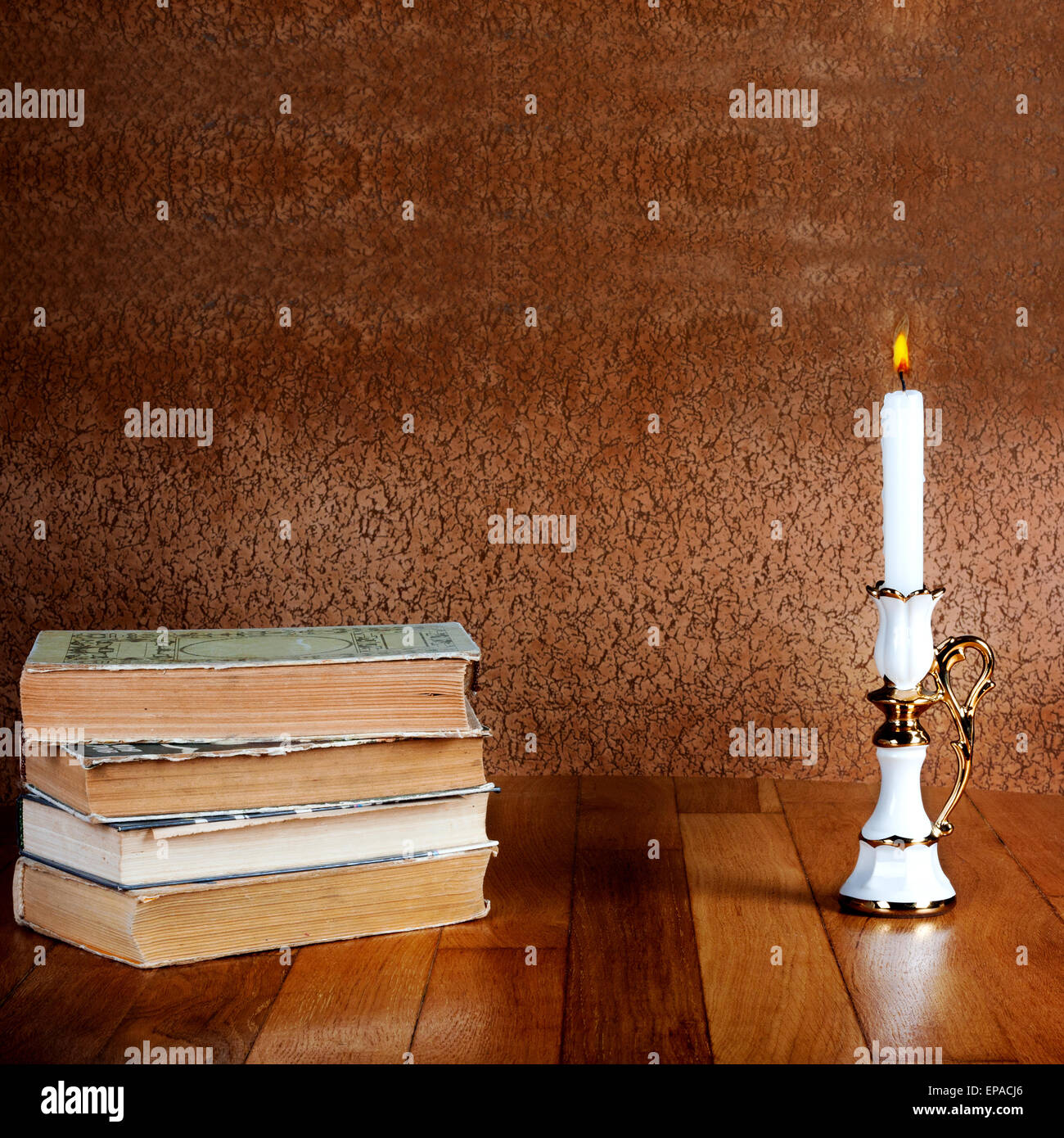 Pila de libros antiguos con candelabro y velas encendidas sobre la mesa de madera Foto de stock