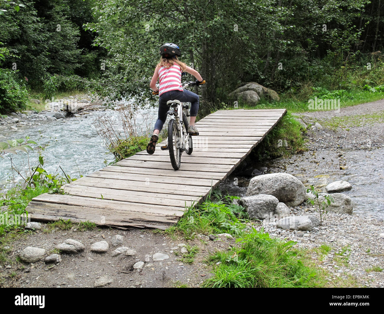 Chica una bicicleta de montaña a través de un puente sobre un arroyo Foto de stock