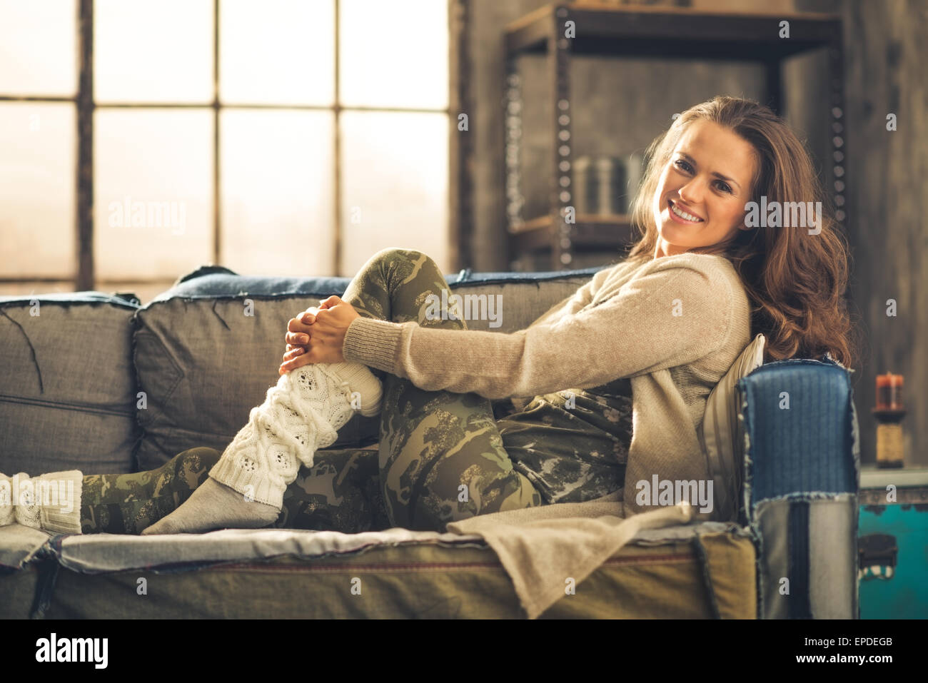 Una elegante mujer sonriente en cómodas, leggings, ropa casual y un cardigan es relajante en un loft sofá. chic industrial y un acogedor Fotografía de stock - Alamy